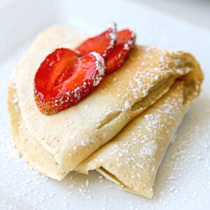 Folded crepe with sliced strawberries on a white plate