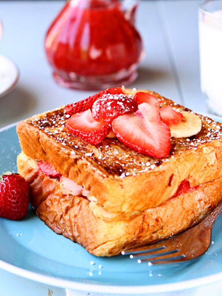Stuffed French toast topped with sliced strawberries and bananas on a blue plate