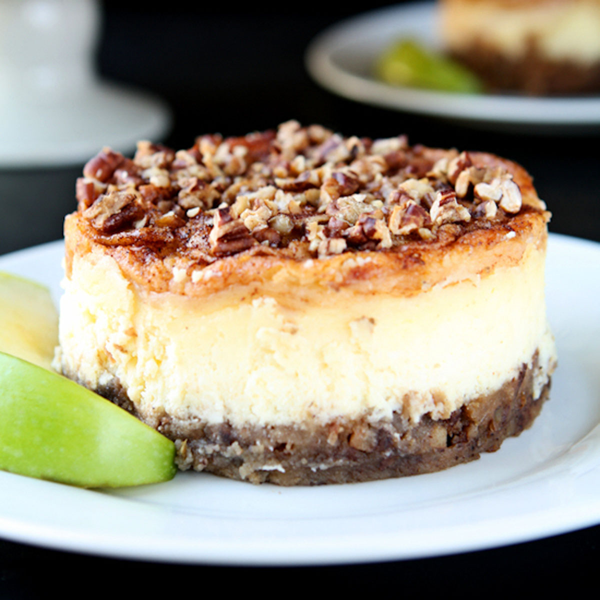 Apple pecan cheesecake on a white plate with apple slices.