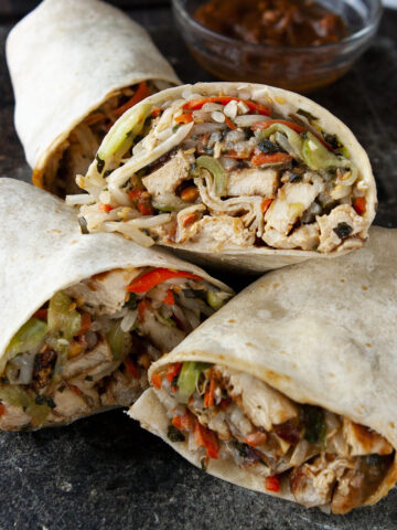 Two chicken wraps cut in half on a dark gray stone surface