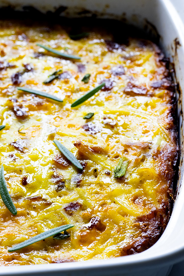 Close up of egg, potato and cheese casserole garnished with rosemary leaves sitting in a white casserole dish