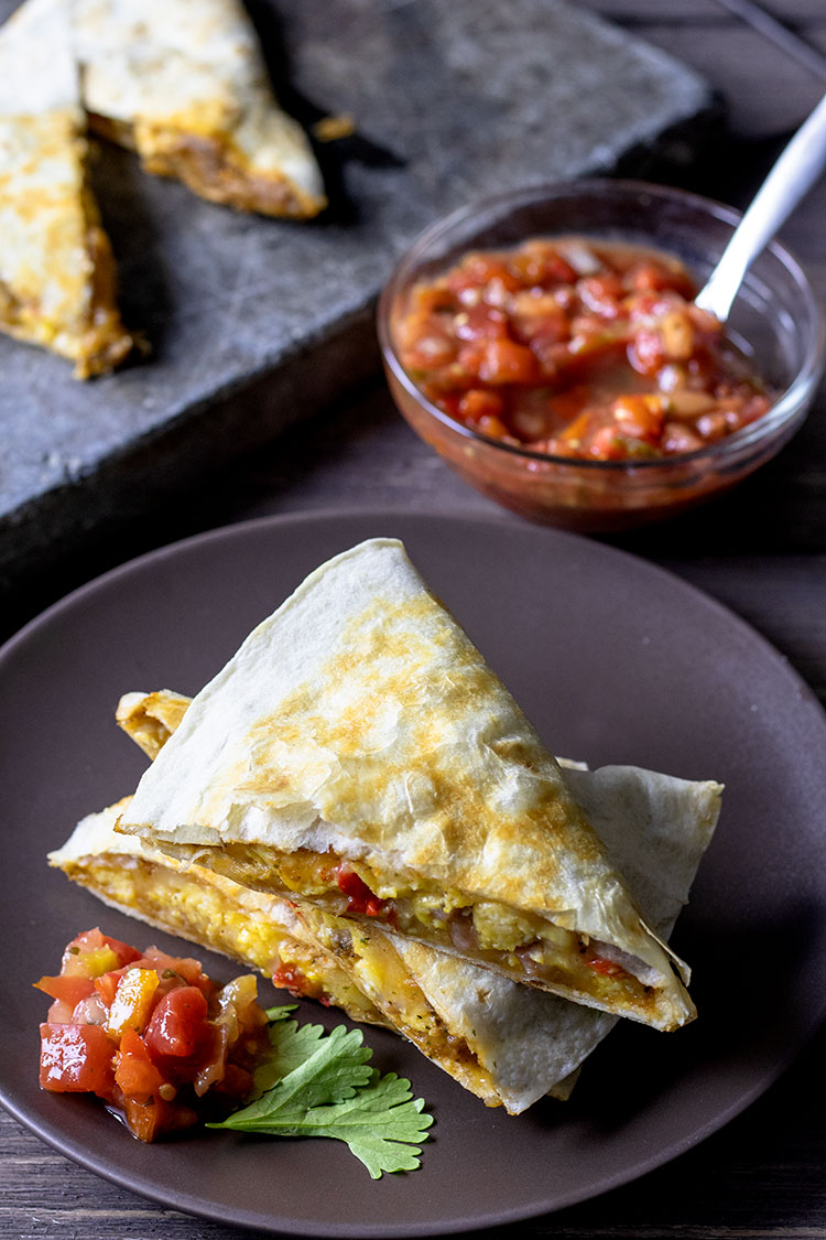 Stacked breakfast quesadilla on a brown plate with salsa