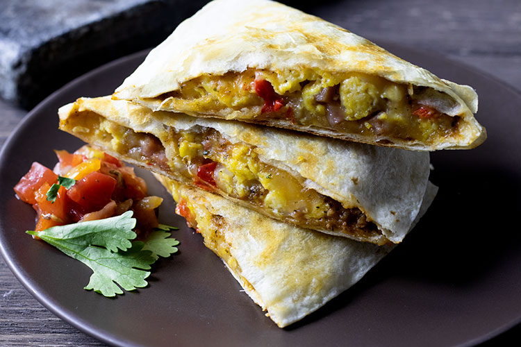 Stacked breakfast quesadillas on a brown plate with salsa and cilantro