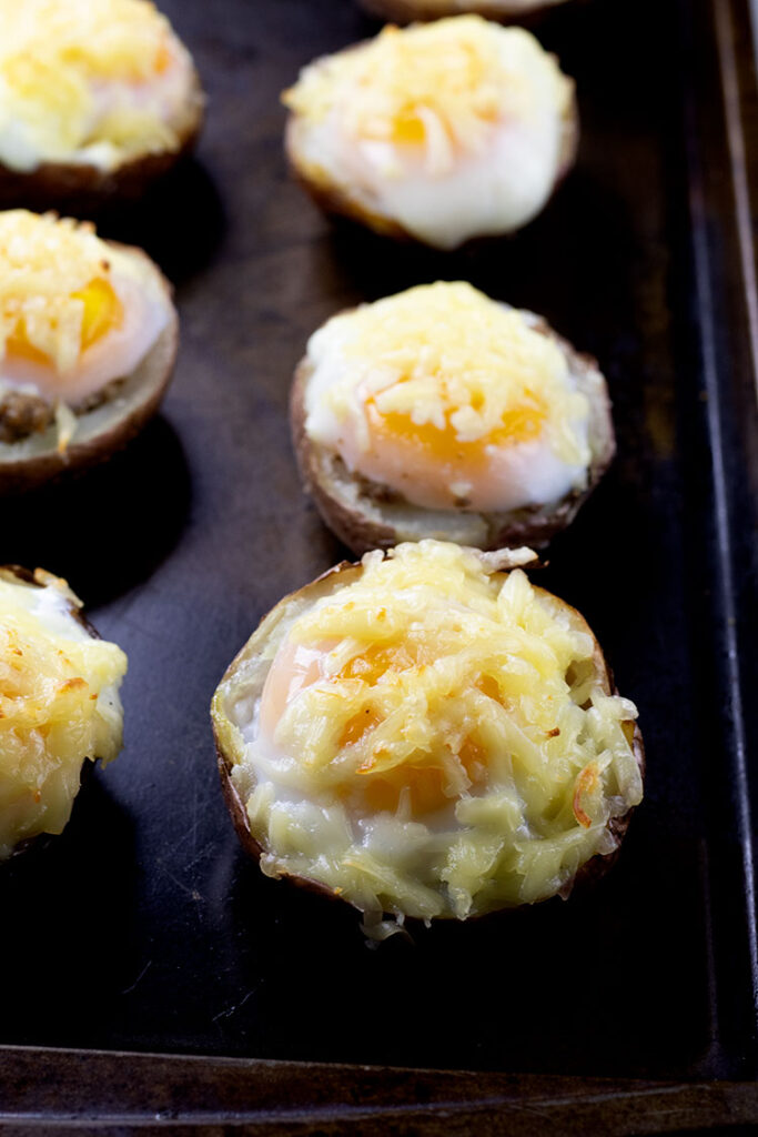 Six potato skins with turkey sausage, poached eggs, and melted cheese sitting on a cookie sheet.