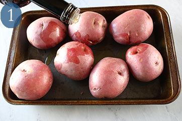 Red potatoes sitting in a baking pan with olive oil being poured over them.