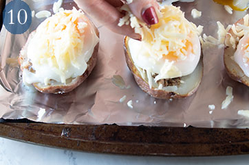 Grated cheese being sprinkled on top of potato skins containing cooked turkey sausage and poached egg.