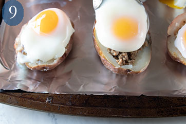 Poached egg being spooned on top of potato skin containing cooked turkey sausage