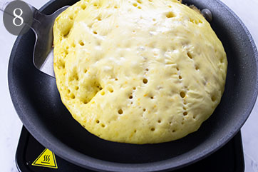 Pancake with popped air holes in a skillet.
