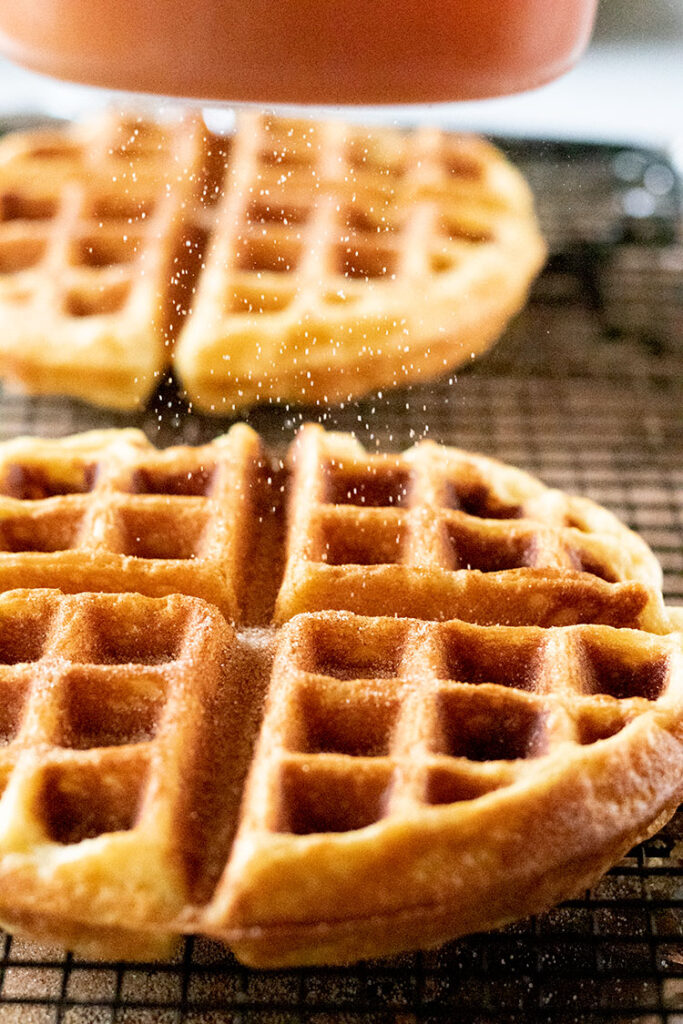 Buttermilk waffles being sprinkled with cinnamon sugar mixture