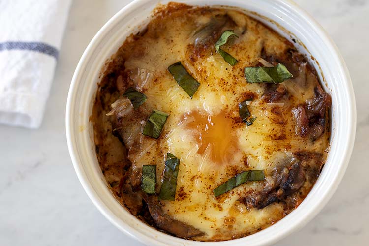 Overhead close up photo of baked eggs with tomato sauce in a white ramekin.