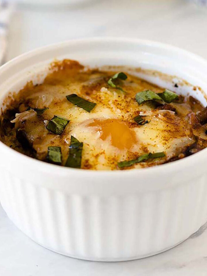 Close up of baked eggs in tomato sauce in a white ramekin.