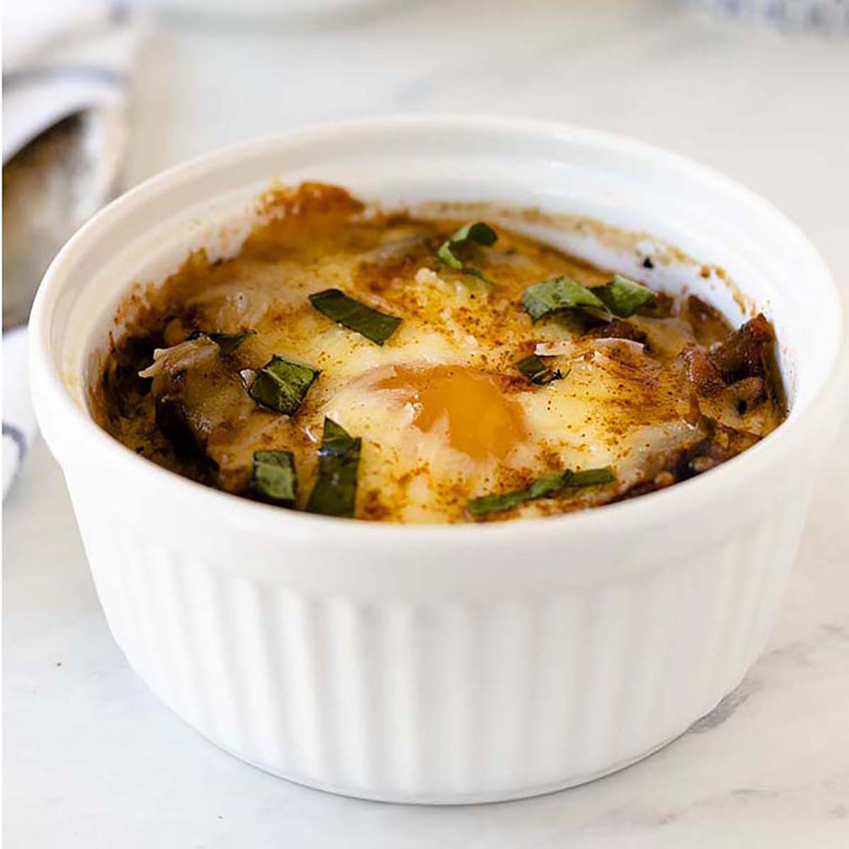 Close up of baked eggs in tomato sauce in a white ramekin.