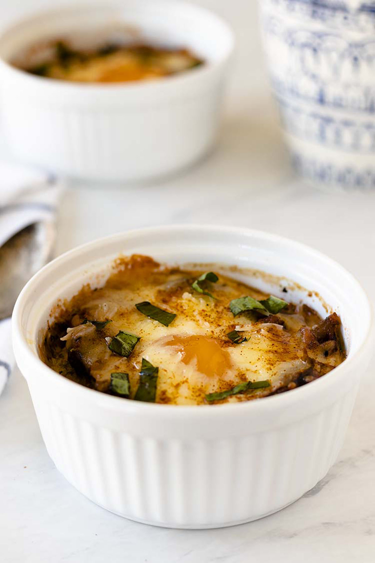 Baked eggs in white ramekins on a marble countertop.