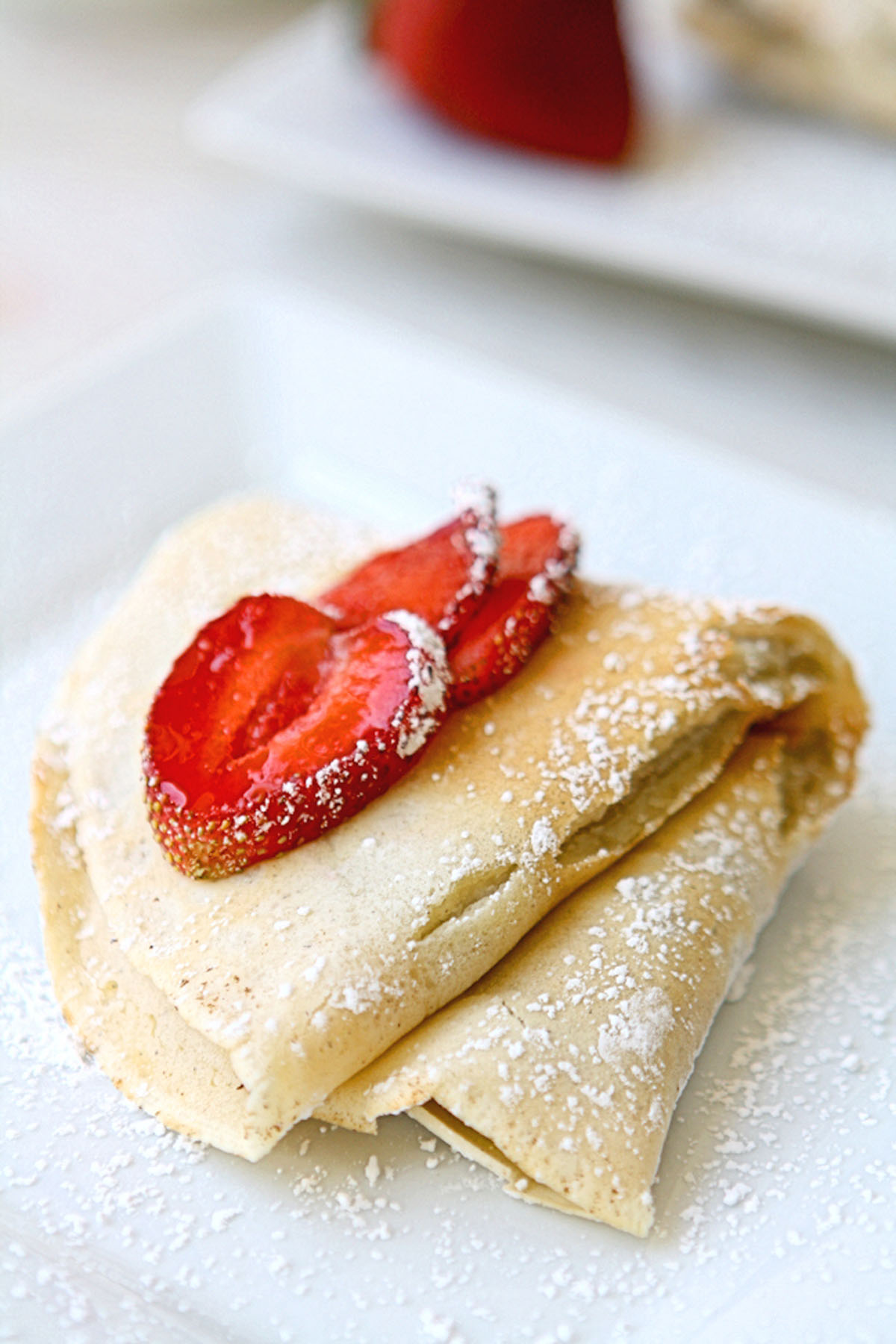 Folded mascarpone crepe topped with sliced strawberries on a white plate