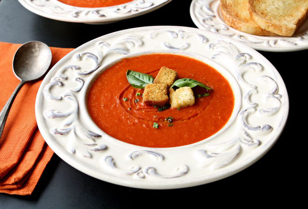 Tomato soup in white bowl ready to serve with a soup spoon to the left of the bowl.