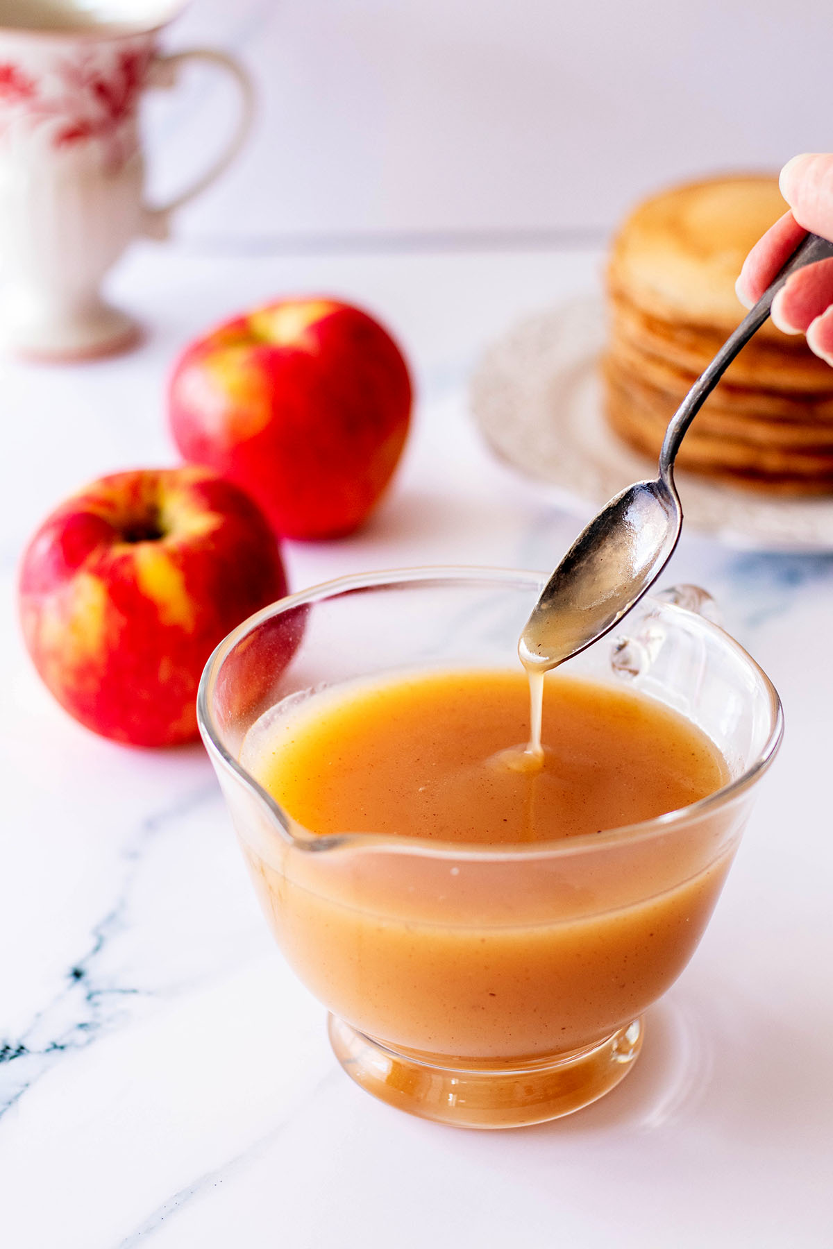 Syrup dripping from spoon into a small glass pitcher