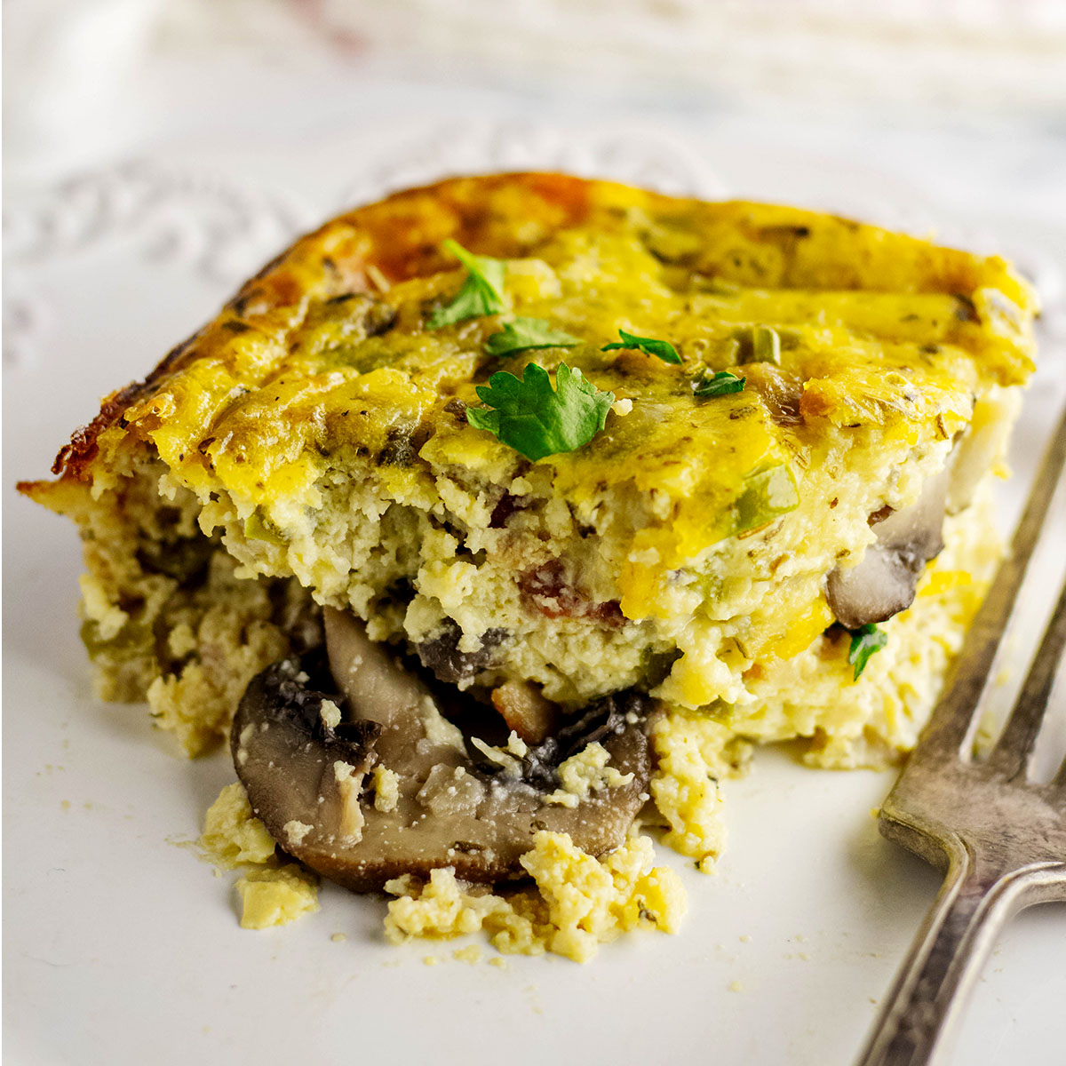 Slice of mushroom breakfast casserole on a white plate with fork