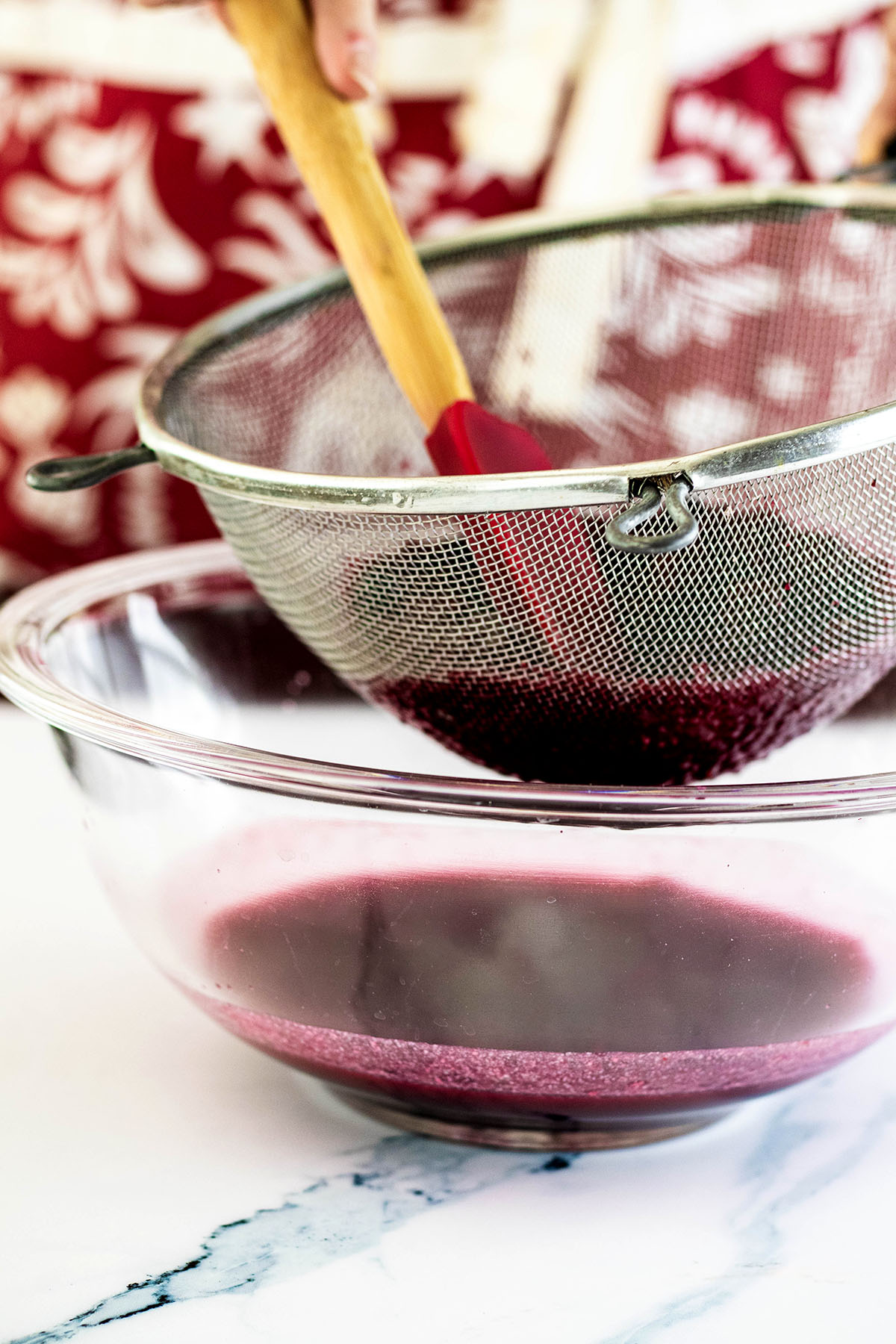 Cooked raspberry syrup being strained through a sieve