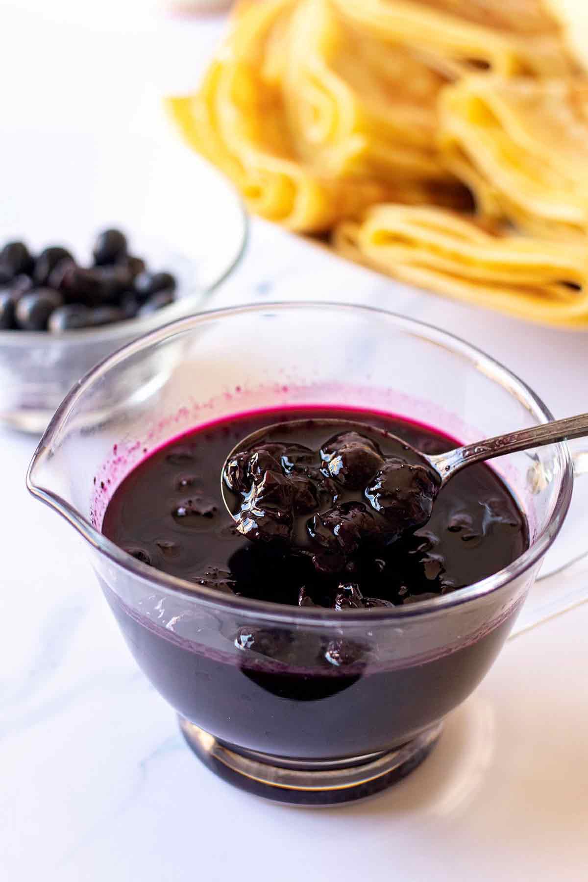 Homemade blueberry syrup in a small glass pitcher with spoon
