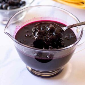 Homemade blueberry syrup in a small glass pitcher with spoon
