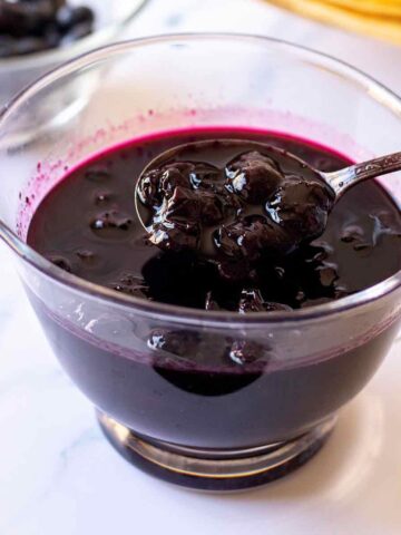 Homemade blueberry syrup in a small glass pitcher with spoon