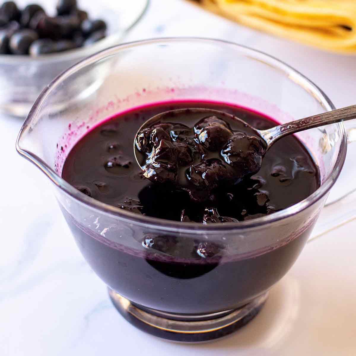 Homemade blueberry syrup in a small glass pitcher with spoon