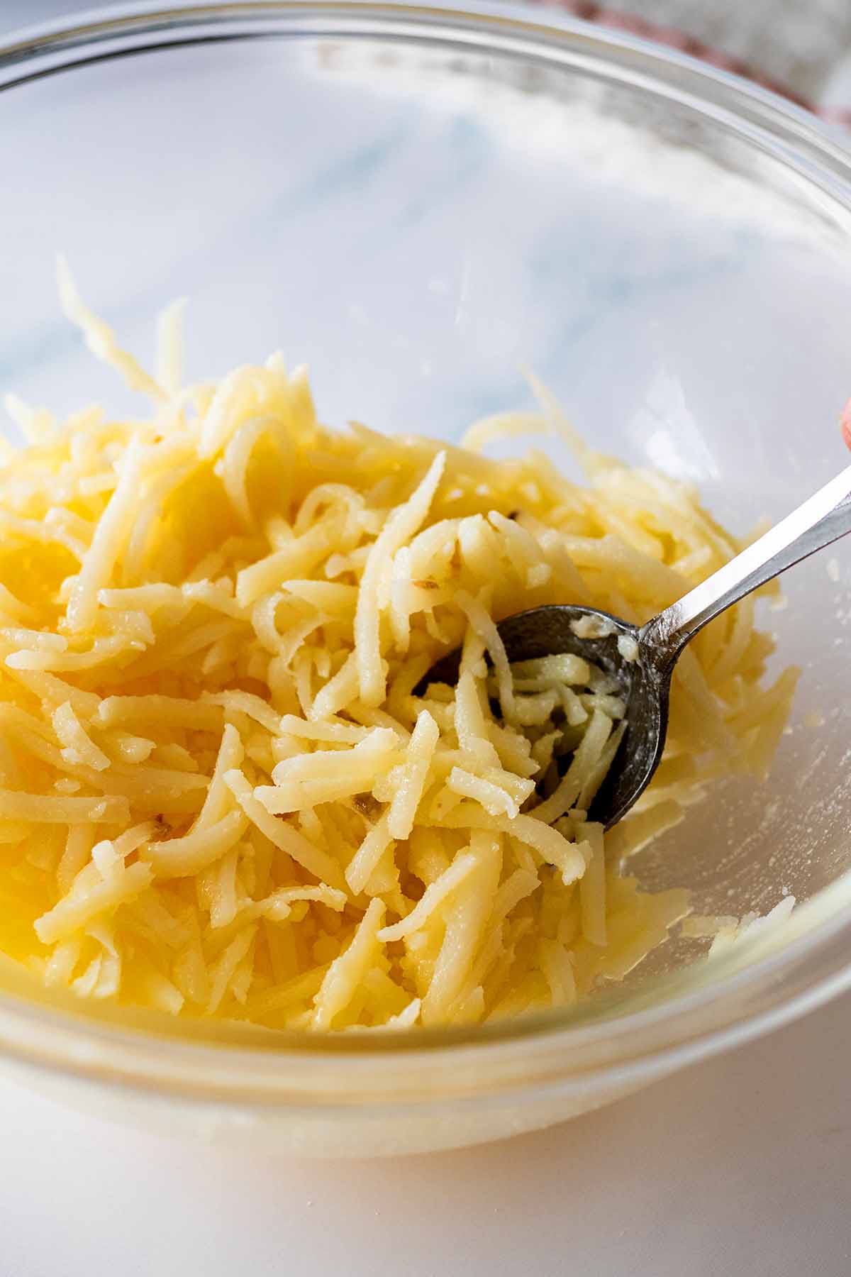 Raw shredded hash brown potatoes in a glass bowl with a spoon
