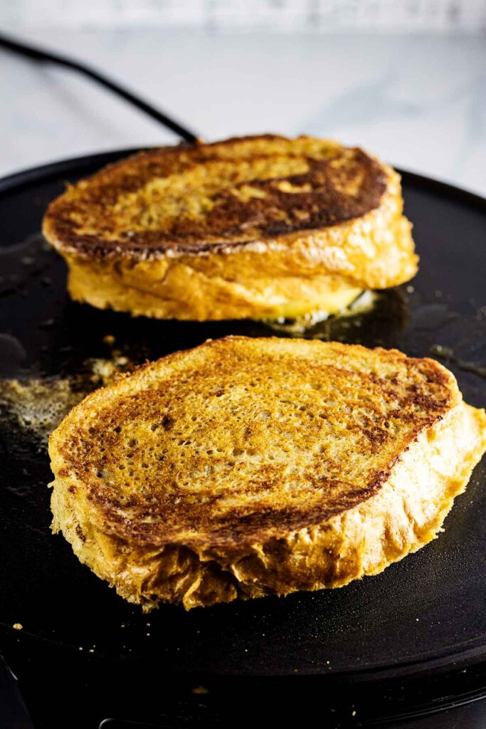 Two slices of caramel apple French toast cooking on a griddle