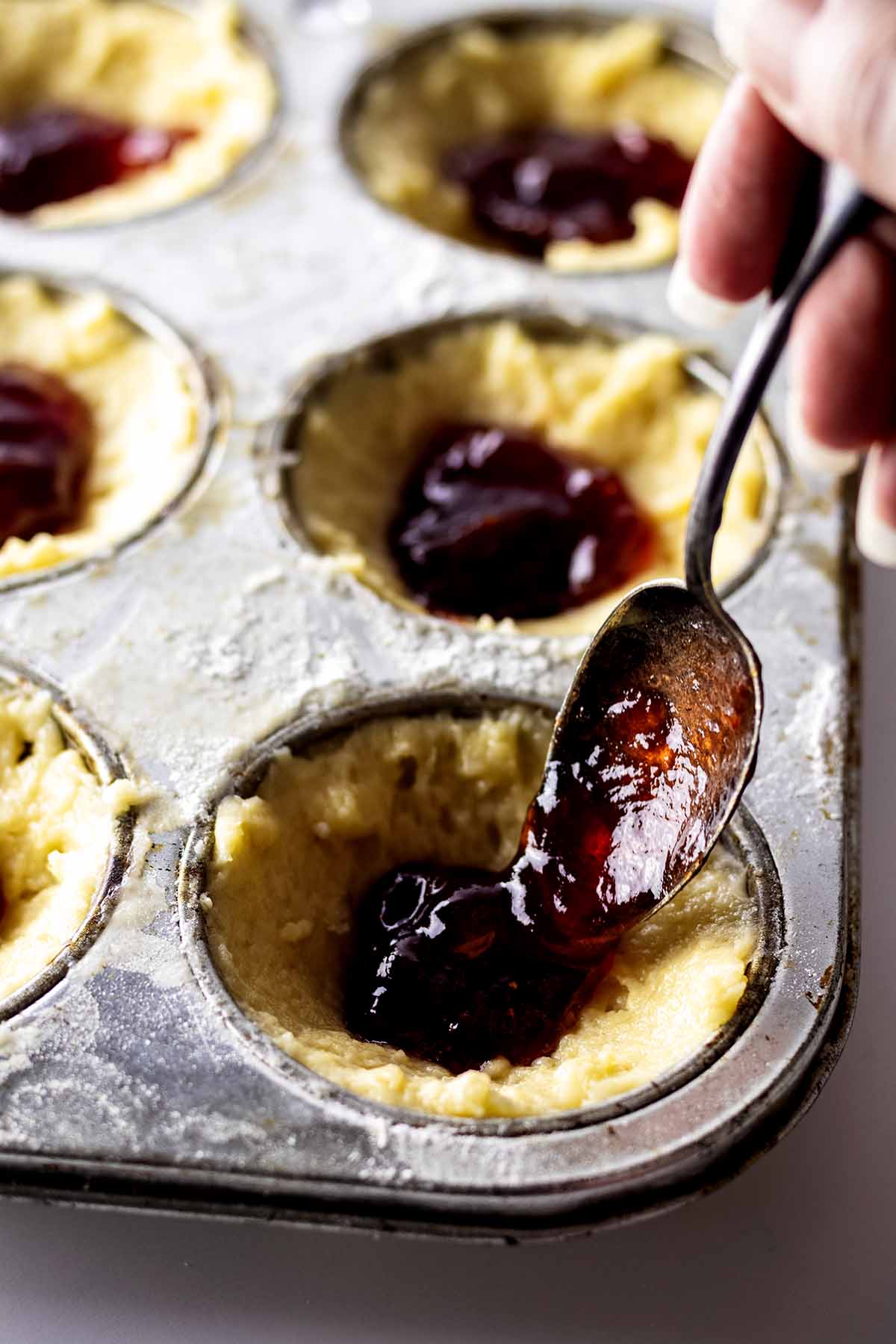 Preserves being spooned over batter in a muffin tin