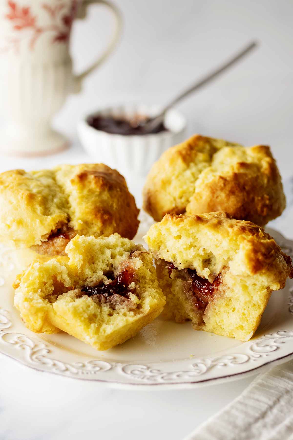 Three biscuit muffins on a white plate with one cut in half exposing the jam inside
