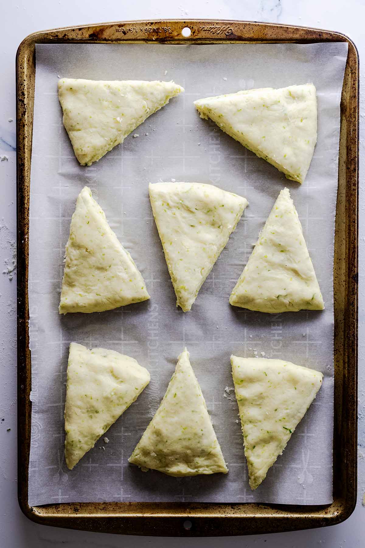Unbaked lime scones on a parchment-lined baking sheet