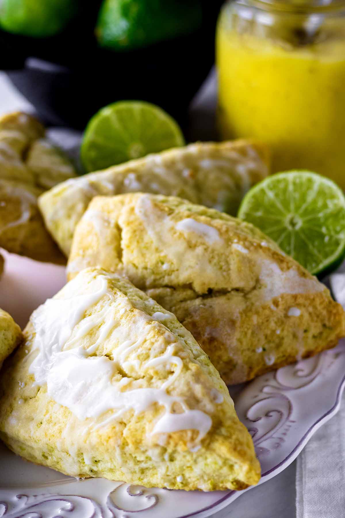 Lime scones on a white plate with limes and a jar of lime curd