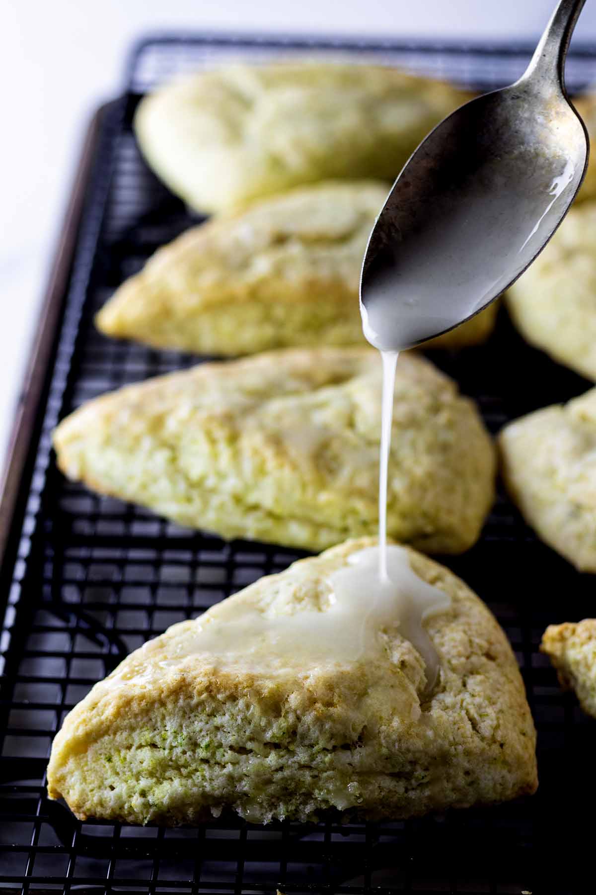 Lime glaze being spooned over baked lime scones on a cooling rack