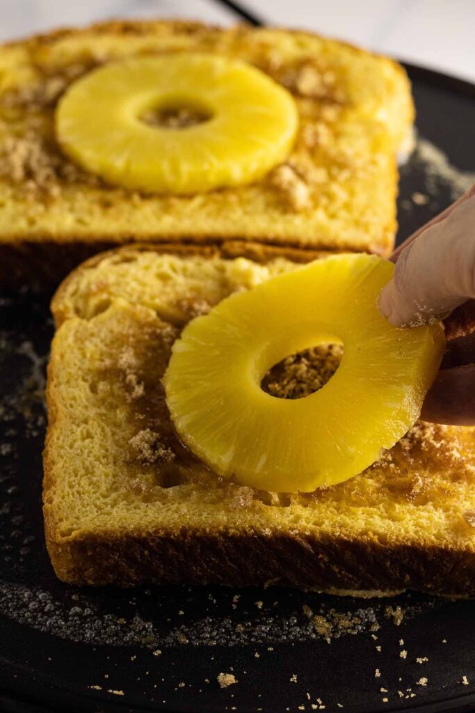 Pineapple rings being placed on bread on griddle
