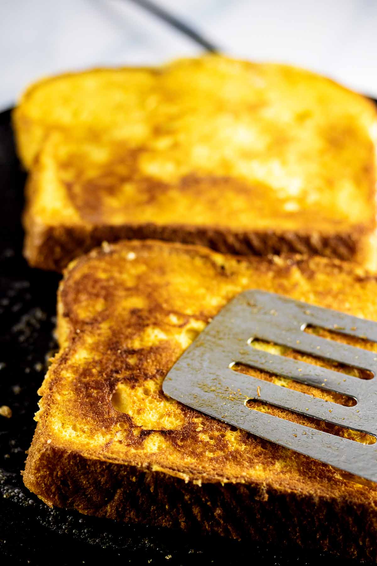 Spatula pressing on slice of golden brown bread on griddle