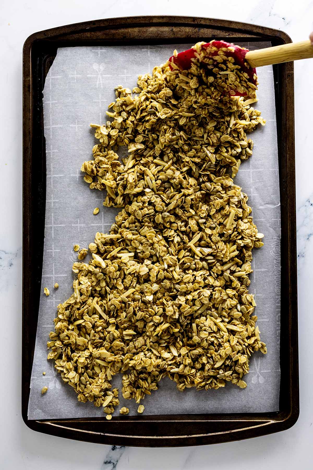 Granola being spread onto a baking sheet with a red spatula