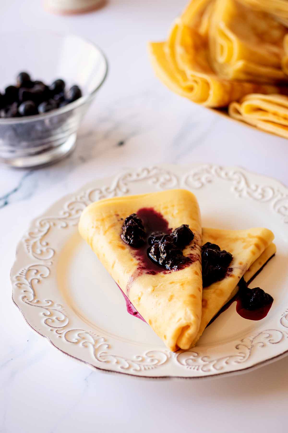 Breakfast crepes topped with blueberry syrup on a white plate.
