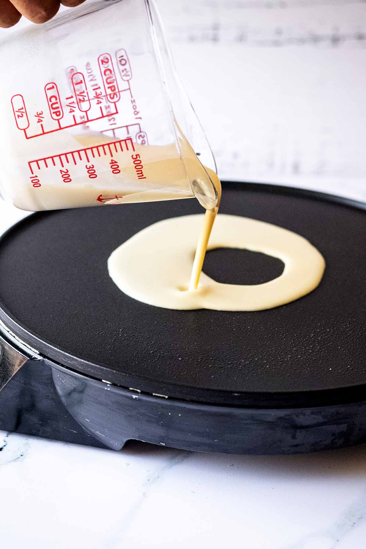 Crepe batter being poured onto a hot griddle