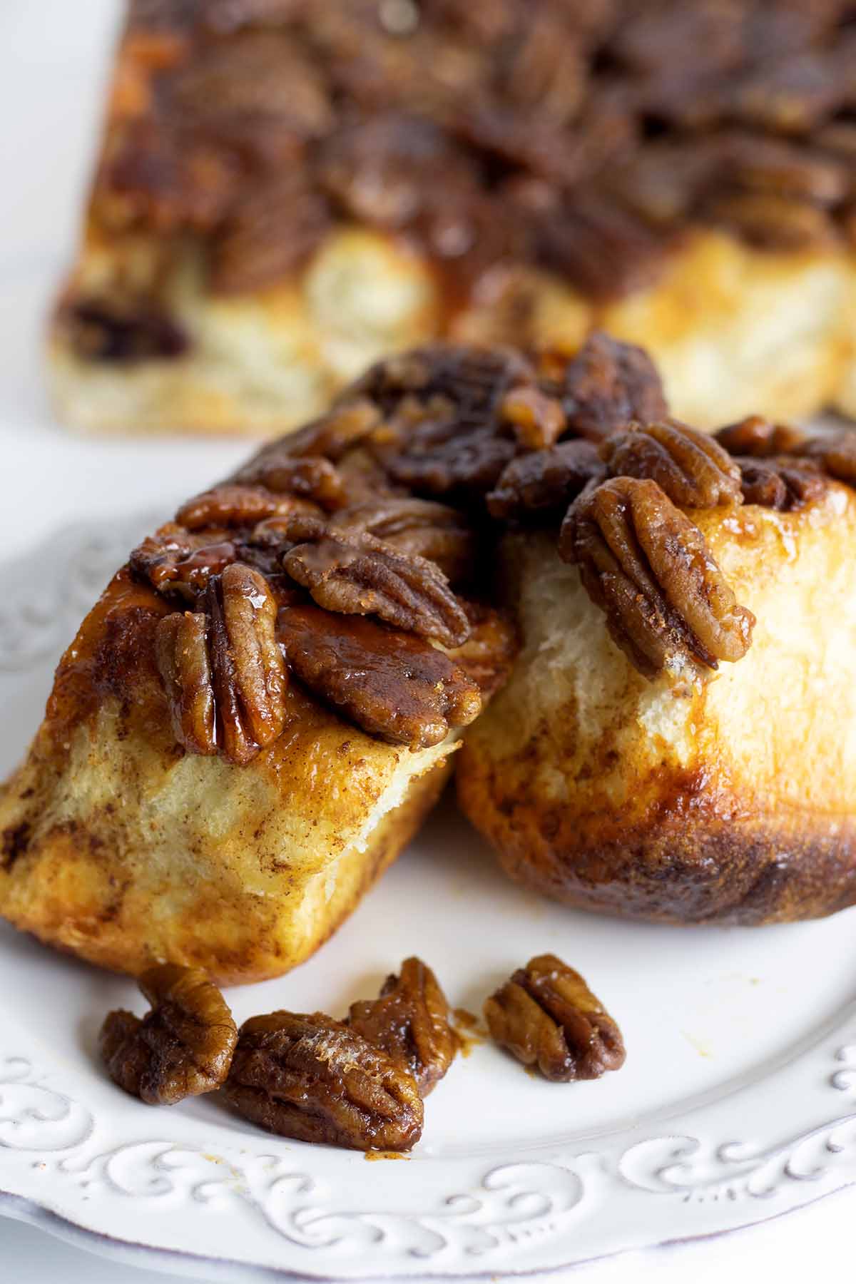 Three caramel pull apart rolls on a white plate with pecans.
