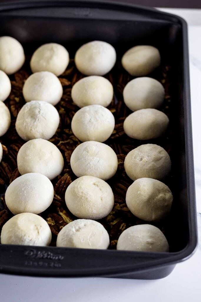 Unbaked rolls lined up in a baking pan.