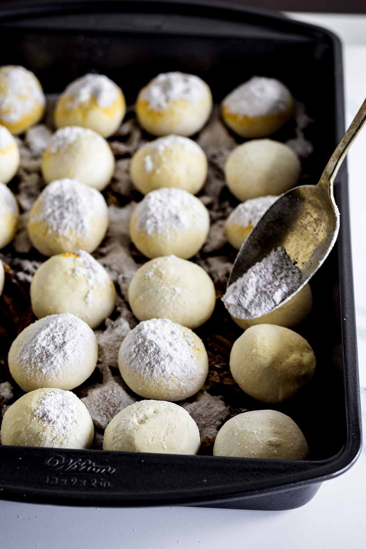Unbaked rolls in a baking pan being sprinkled with butterscotch pudding mix