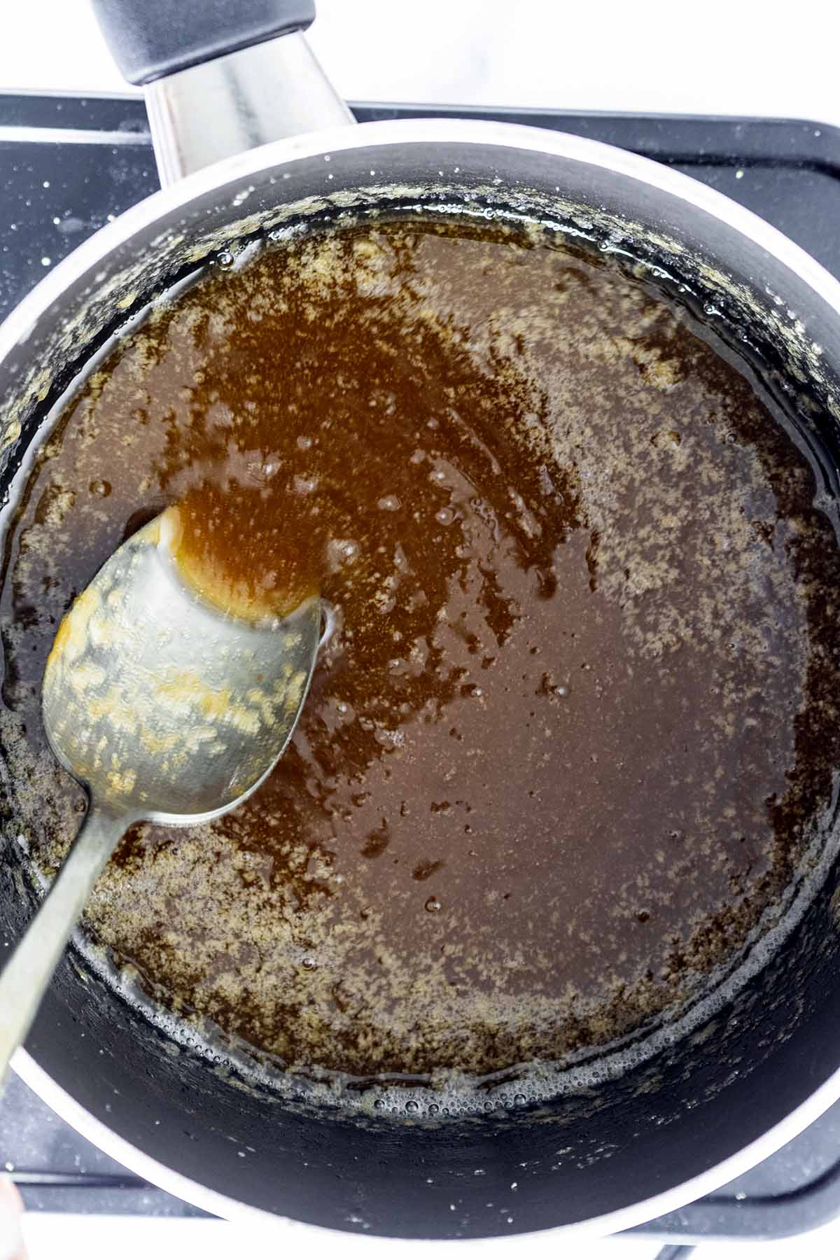 Caramel sauce cooking in a saucepan with a spoon