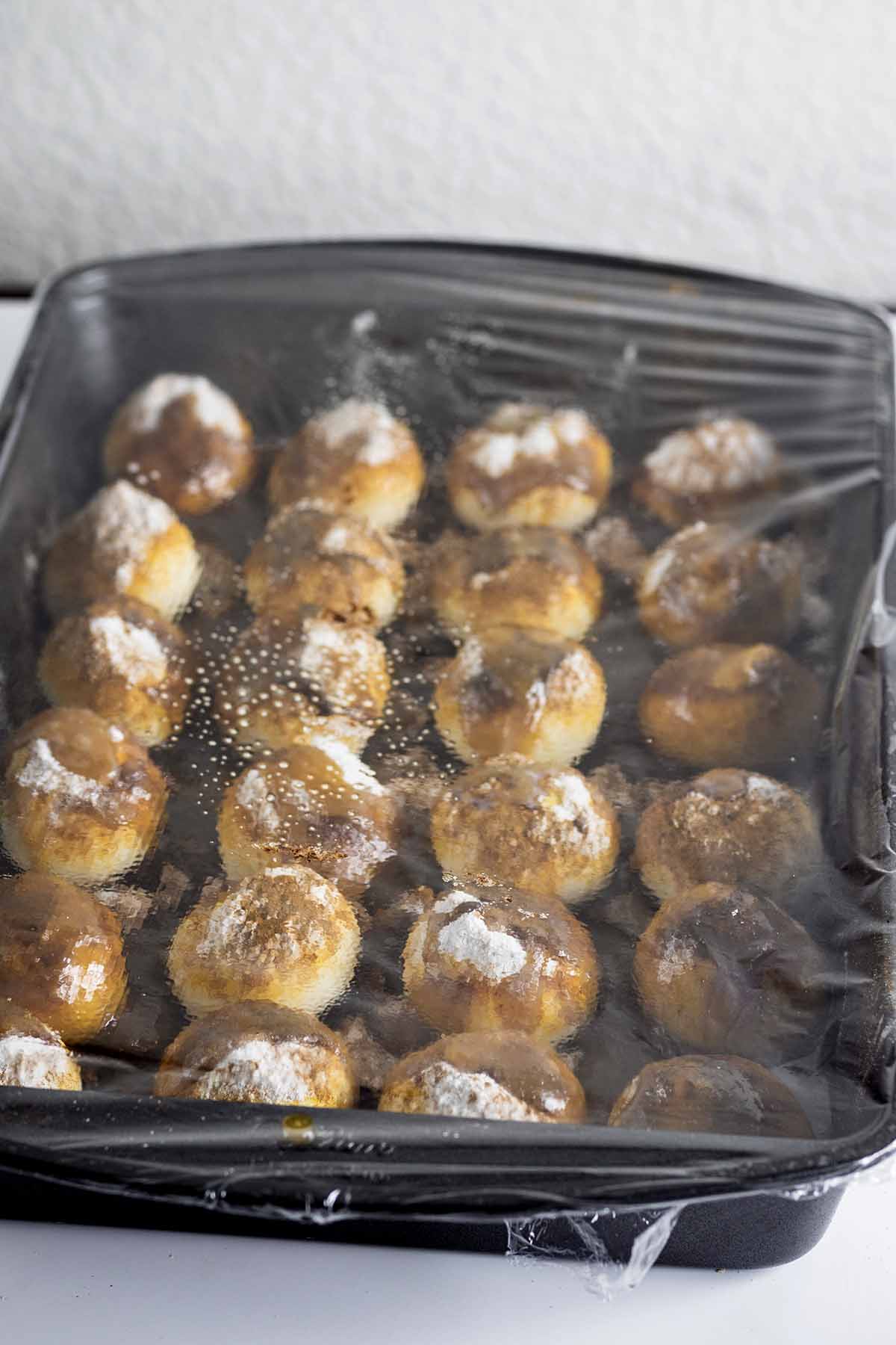 Unbaked rolls in a baking pan covered with plastic wrap