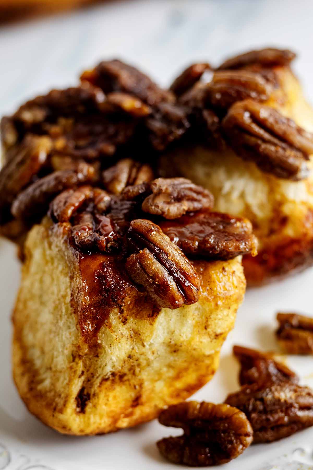 Close up of a pecan-topped pull apart roll on a white plate.
