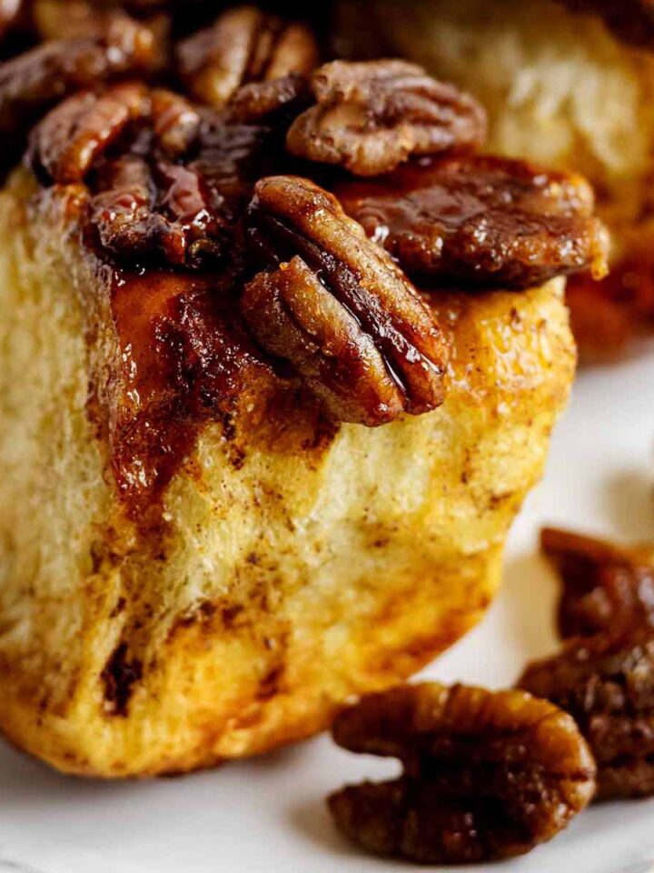 Close up of a pecan-topped pull apart roll on a white plate.