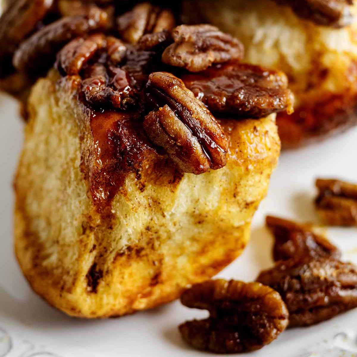 Close up of a pecan-topped pull apart roll on a white plate.