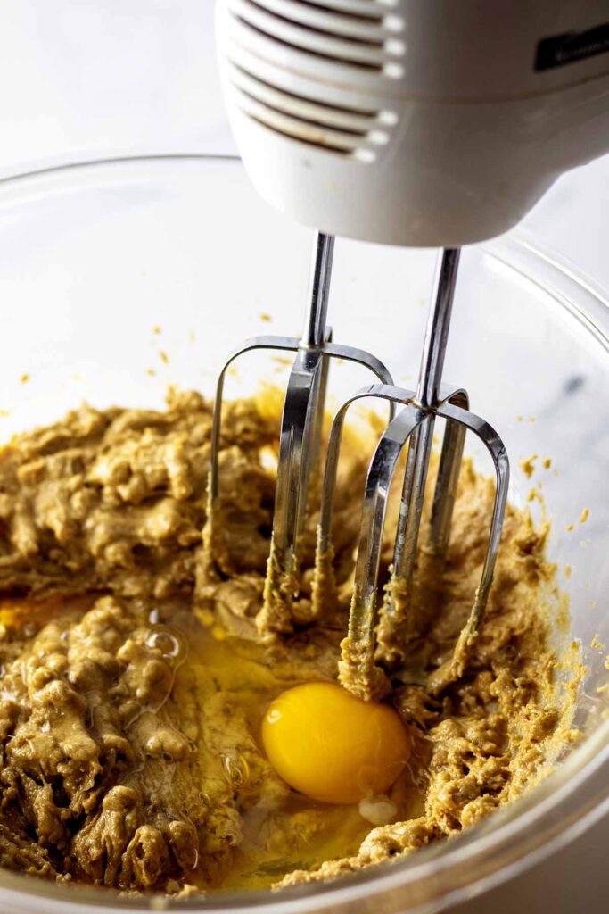 Electric mixer and batter in a glass bowl with a raw egg