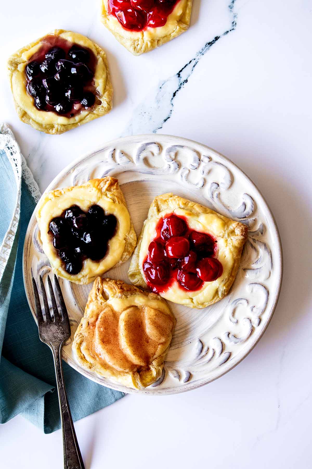 Overhead view of breakfast pastries on a white plate with a fork and blue napkin