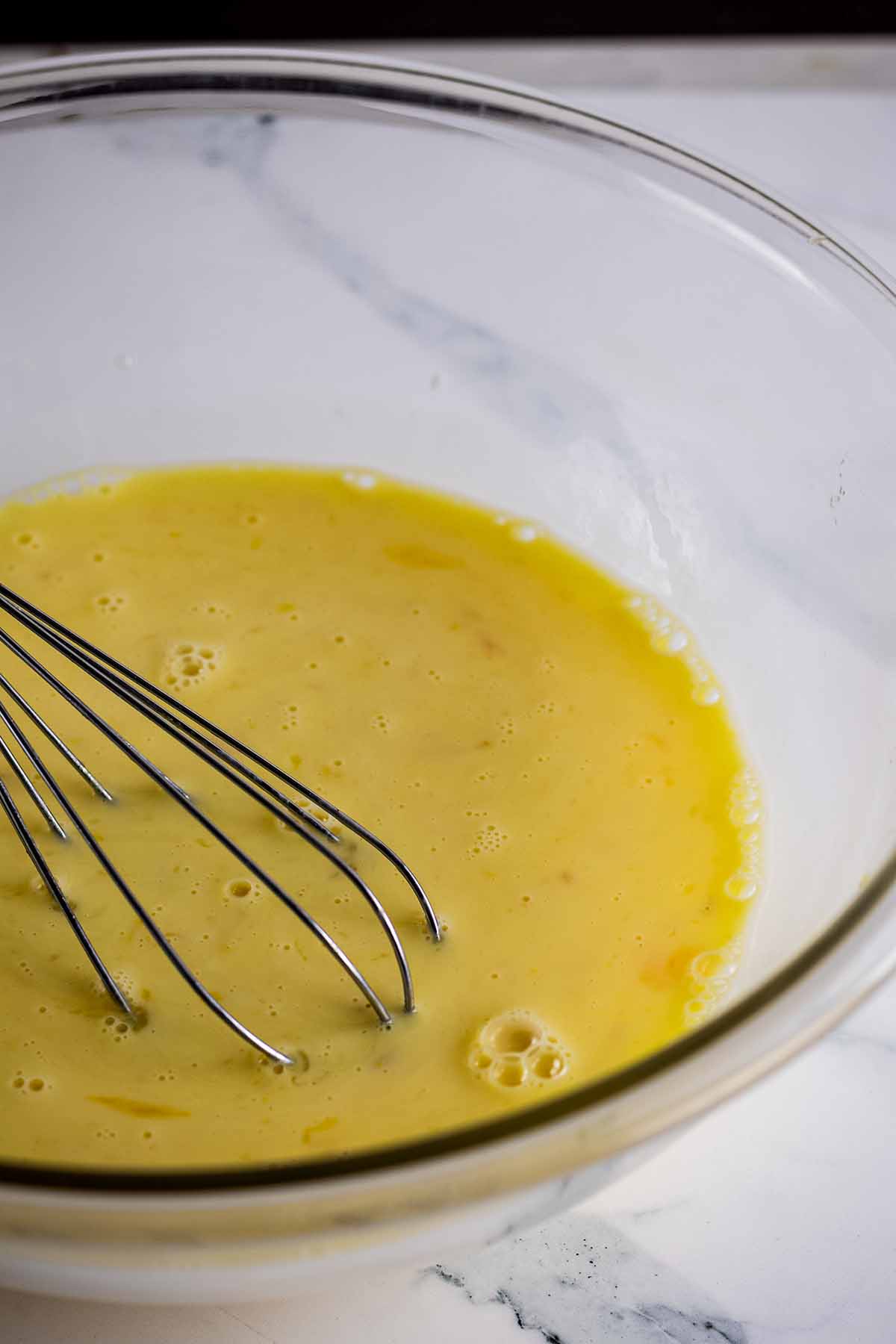 Egg mixture in a glass bowl with a whisk
