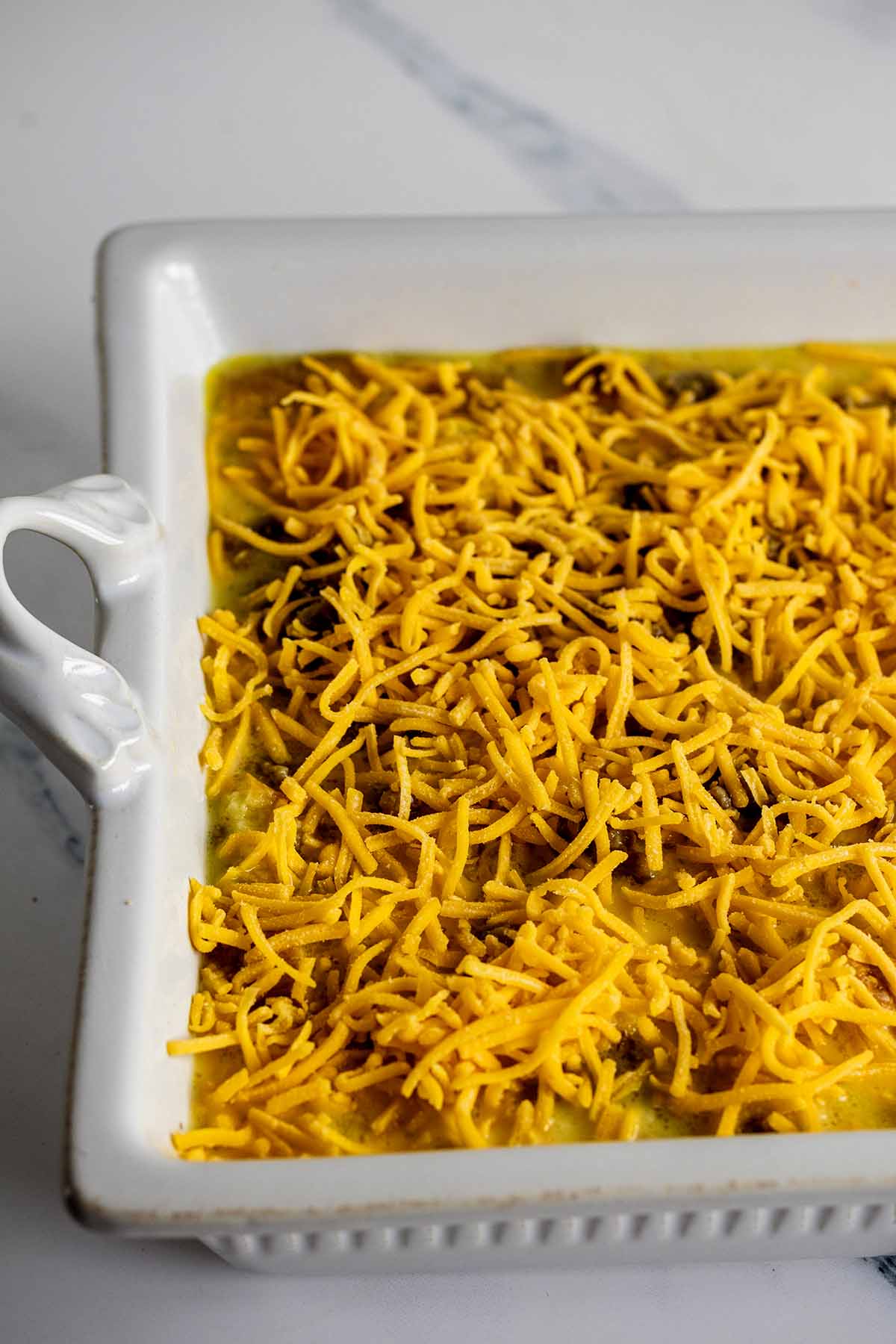 Shredded yellow cheddar cheese sprinkled on top of unbaked breakfast casserole